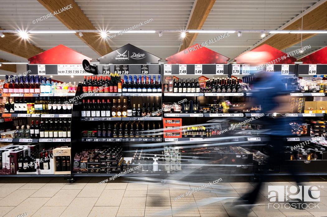 Stock Photo: PRODUCTION - 15 December 2021, North Rhine-Westphalia, Kaarst: A man walks his shopping trolley past shelves of Sansibar and deluxe products in a Lidl store.