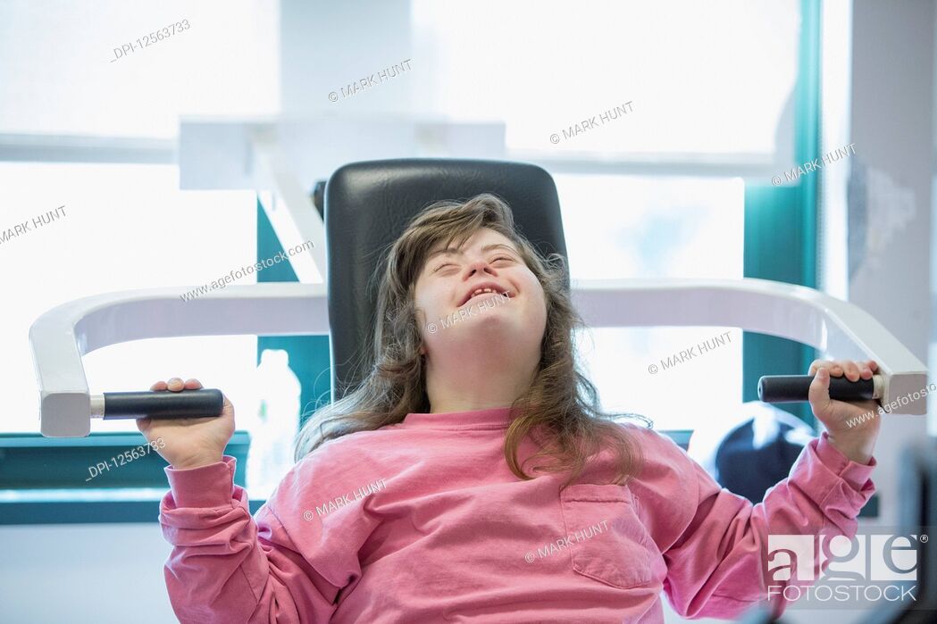 Stock Photo: Young woman with Down Syndrome working out on an exercise machine in gym.