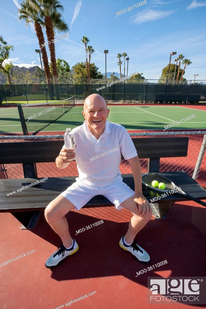 Stock Photo: Portrait of happy senior male tennis player with water bottle relaxing on court.