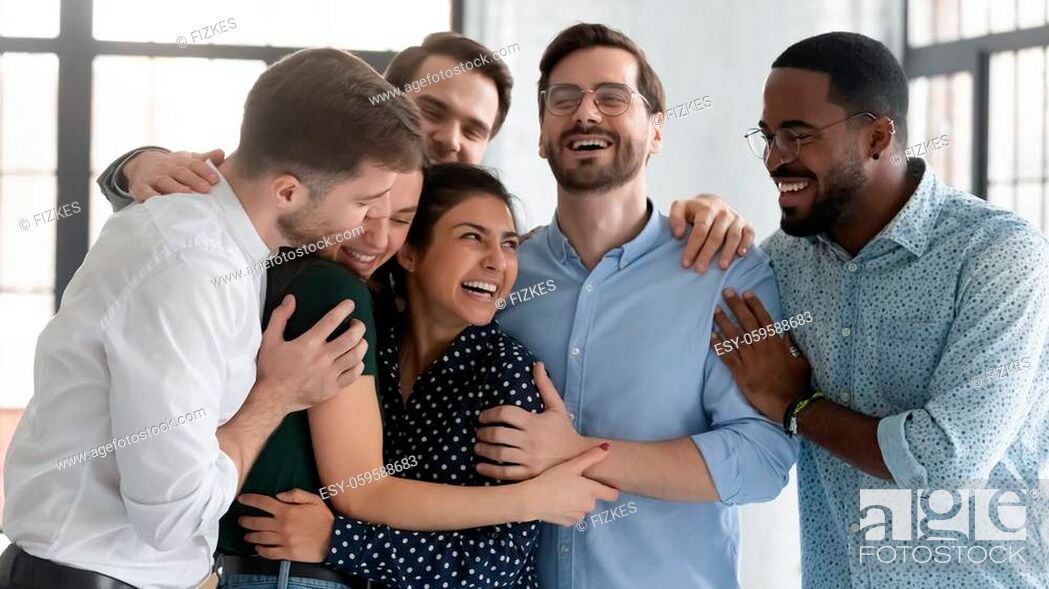 Stock Photo: Overjoyed multiracial colleagues have fun laugh celebrate shared win or victory at workplace, happy diverse multiethnic coworkers hug show unity and support at.