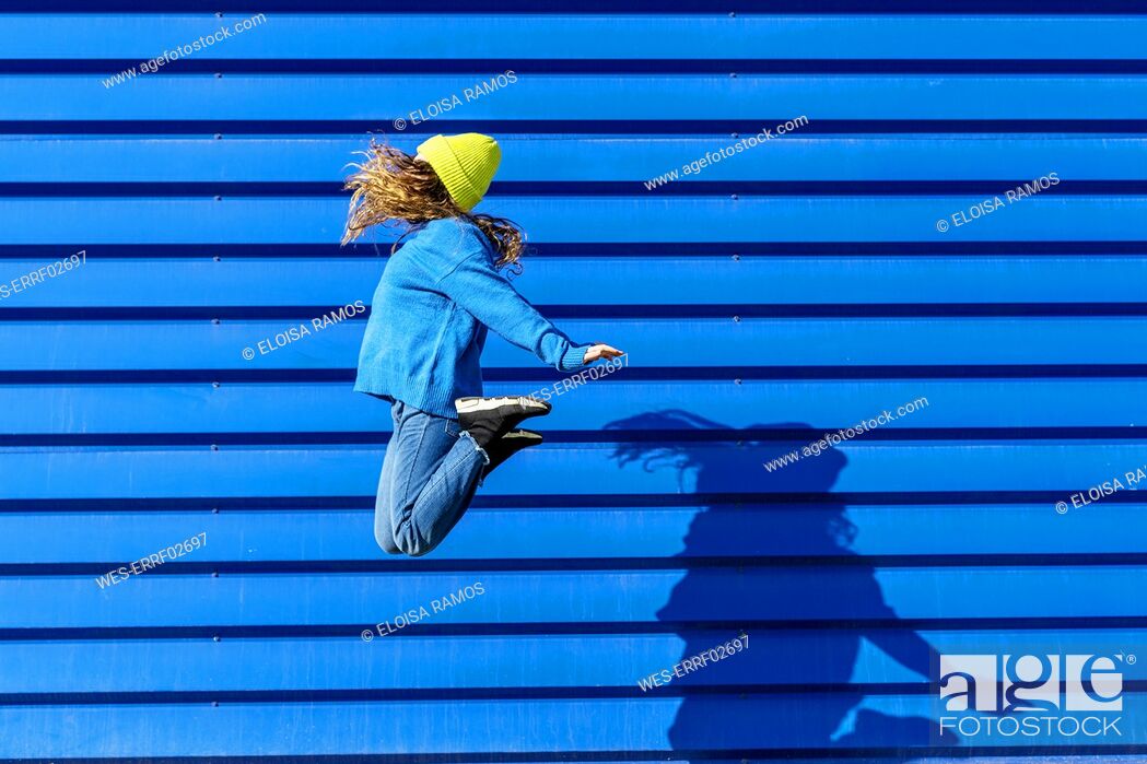 Stock Photo: Teenage girl jumping in the air in front of blue background.