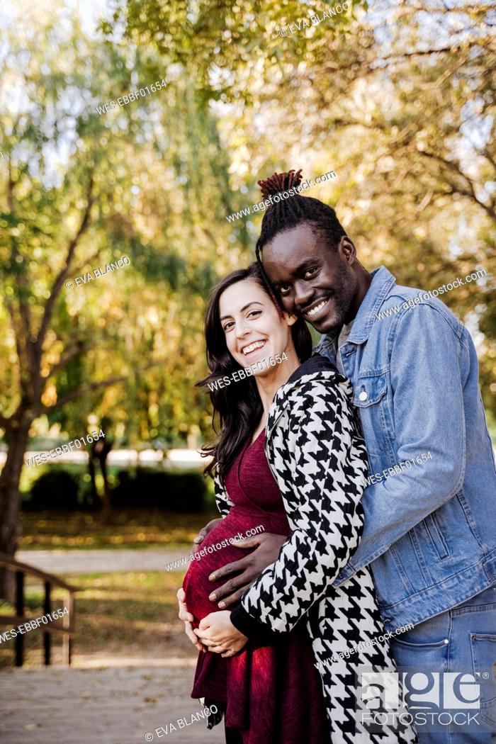 Stock Photo: Happy pregnant woman standing with man in park.