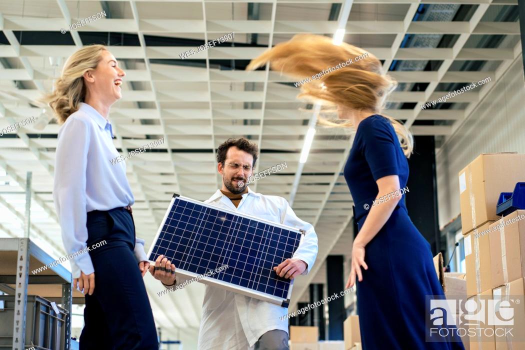 Stock Photo: Carefree businessman playing with solar panel by colleagues at warehouse.