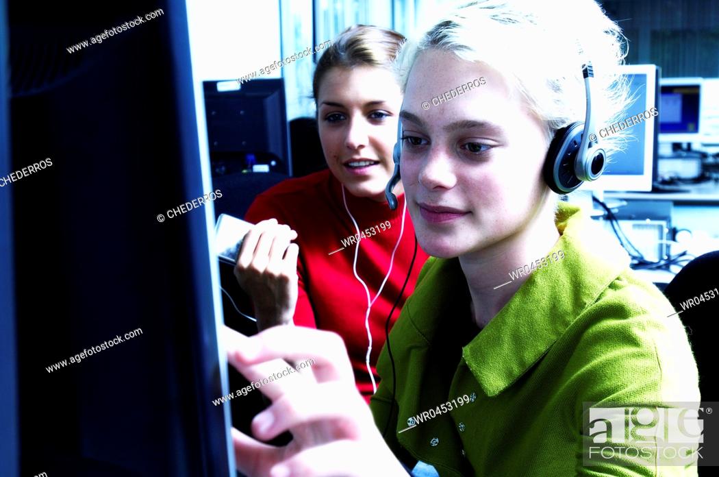 Stock Photo: Teenage girl wearing a headset using a computer with another teenage girl sitting beside her.