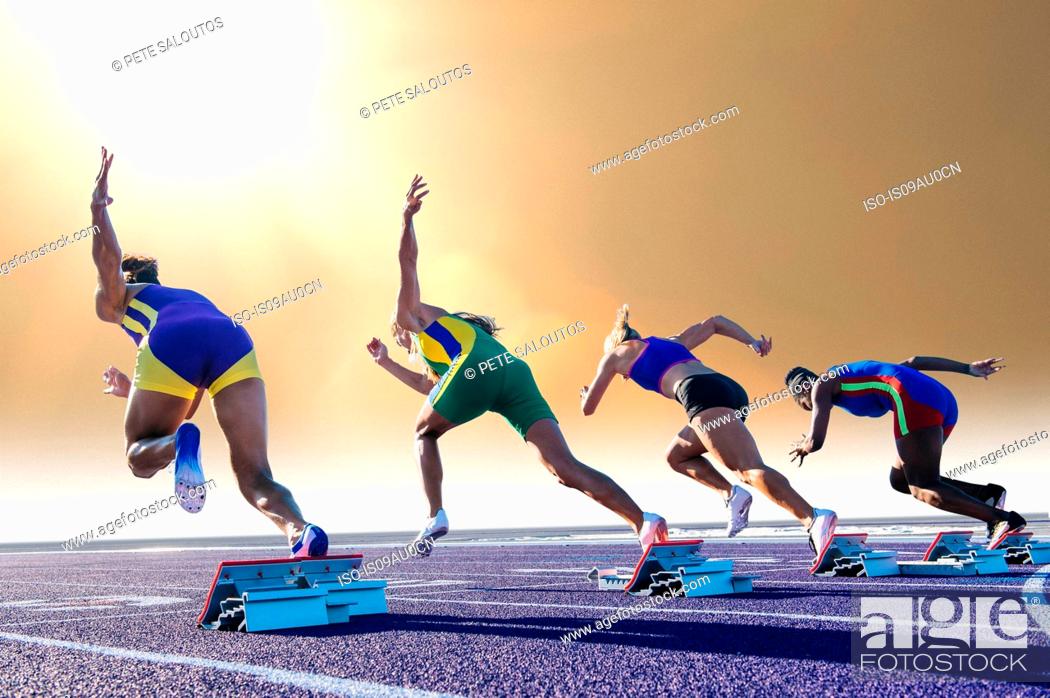 Stock Photo: Four female athletes on athletics track, leaving starting blocks, rear view.