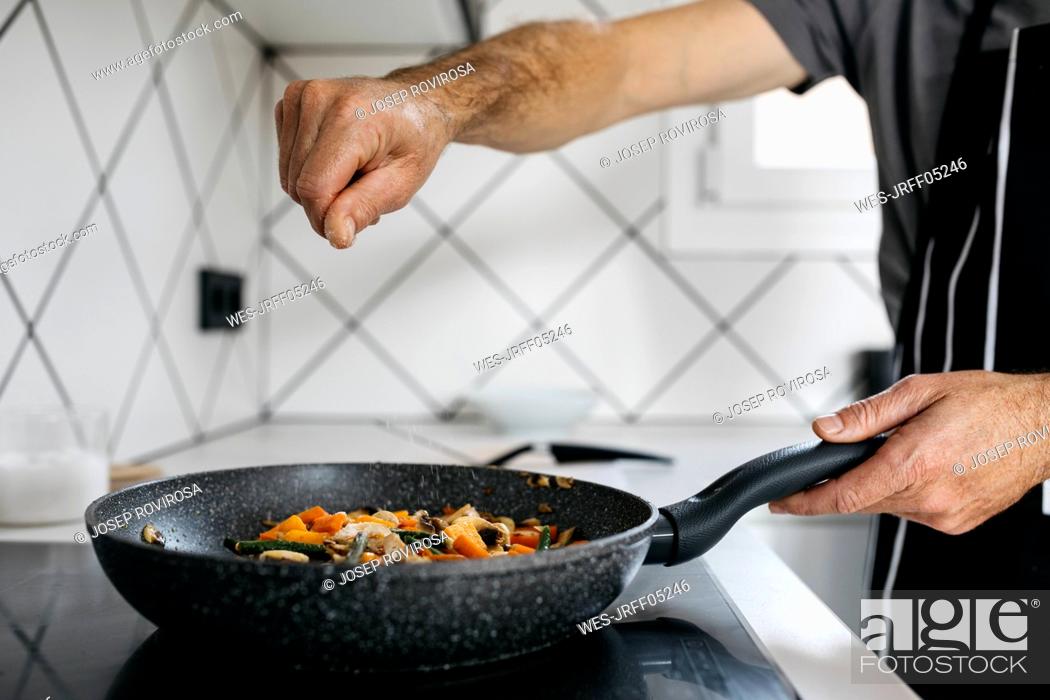 Stock Photo: Man sprinkling salt on vegetables in frying pan.