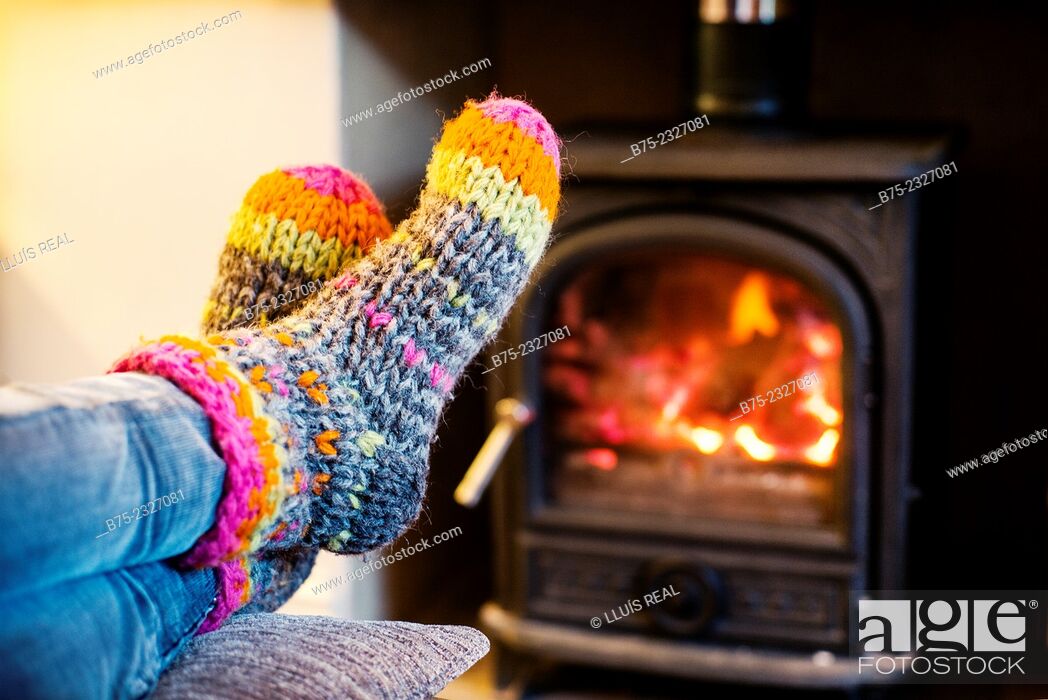 Stock Photo: Feet warming up with a hand made colored socks in a position of rest and relax near a wood stove in winter.