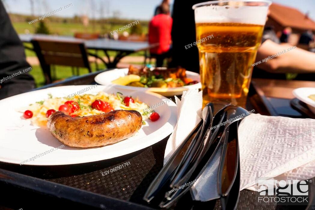 Stock Photo: Sausage with salad on a plate and light beer on a tray. Street food and beer festival on a sunny day. Food for a friendly campaign and a picnic in nature.