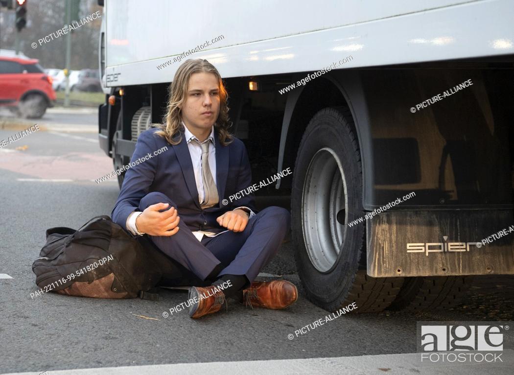 Stock Photo: 16 November 2022, Berlin: An activist from the group ""Last Generation"" sits at an intersection on Landsberger Allee while a truck tries to pass him.