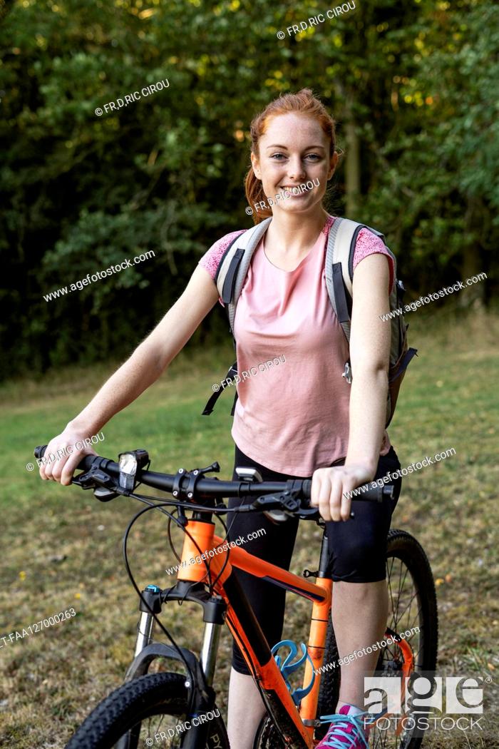 Imagen: Smiling young woman sitting on bicycle in forest.
