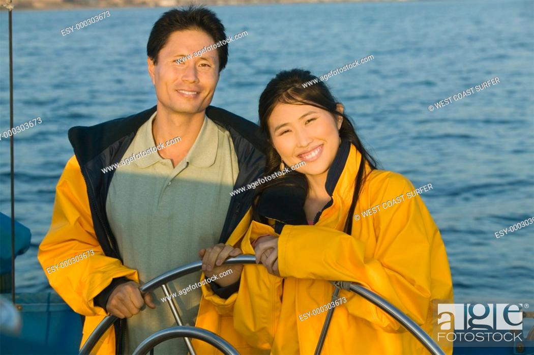 Photo de stock: Couple wearing yellow anoraks at steering wheel of sailboat portrait.