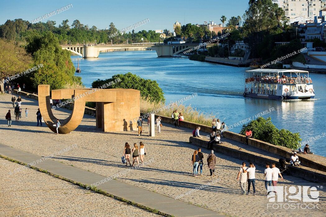 Stock Photo: Spain, Andalucia, Sevilla, people walking by the riverside of the Guadalquivir river below the Paseo de Cristobal Colon.