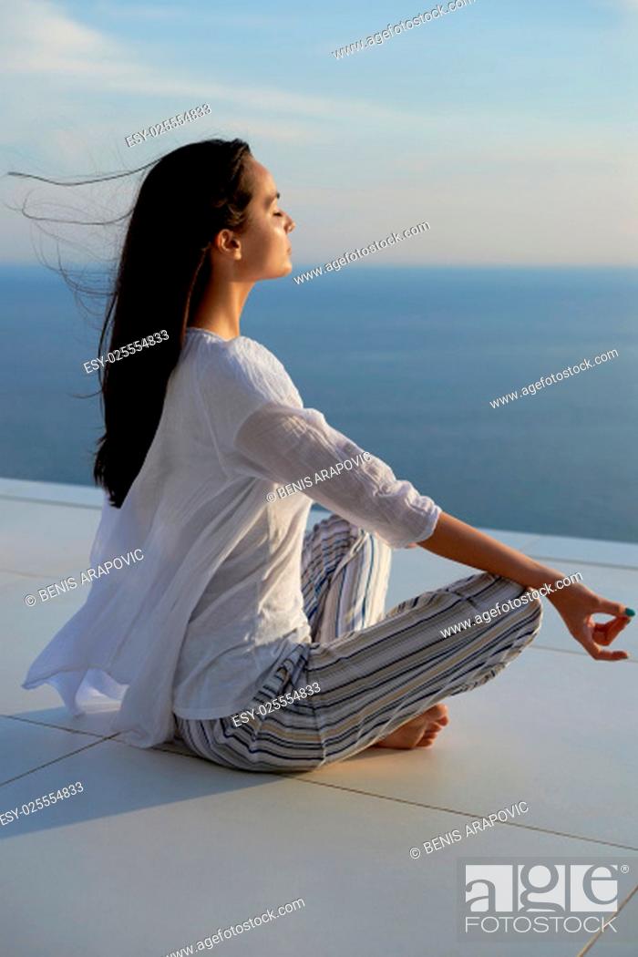 Stock Photo: young woman practice yoga meditaion on sunset with ocean view in background.