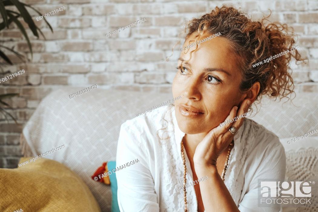 Stock Photo: Portrait of serene woman looking outside the window at home having relax time sitting on the couch. Happy and confident female people front view.