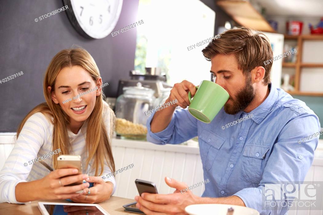 Stock Photo: Young Couple Eating Breakfast Whilst Using Mobile Phones.