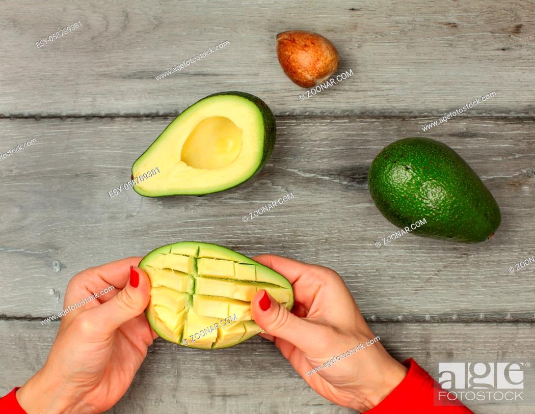 Stock Photo: Tabletop view on woman hands preparing avocado, getting out the pulp cut in squares.