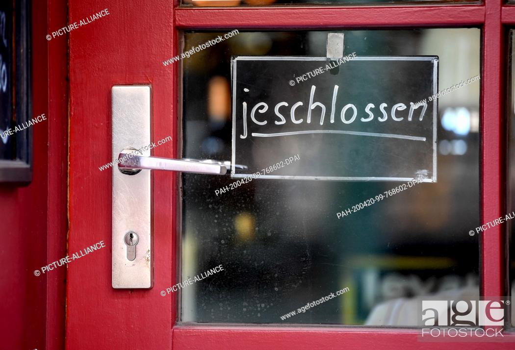 Stock Photo: 20 April 2020, Berlin: A sign on the entrance door of a pub with the inscription ""jeschlossen"" (closed) indicates that the locality has closed.