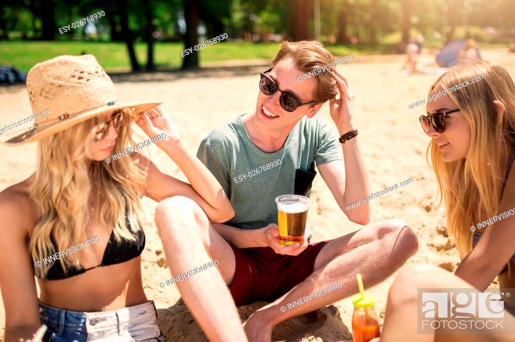 Stock Photo: A photo of man and two girls sitting on the beach with drinks and talking.