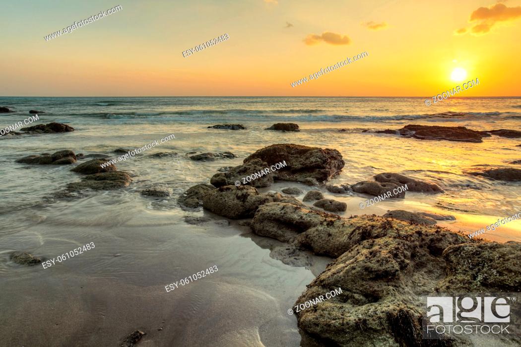 Stock Photo: Beach in low tide, sand and rocks covered with algae showing from water, during golden sunset light. Koh Lanta, Thailand.