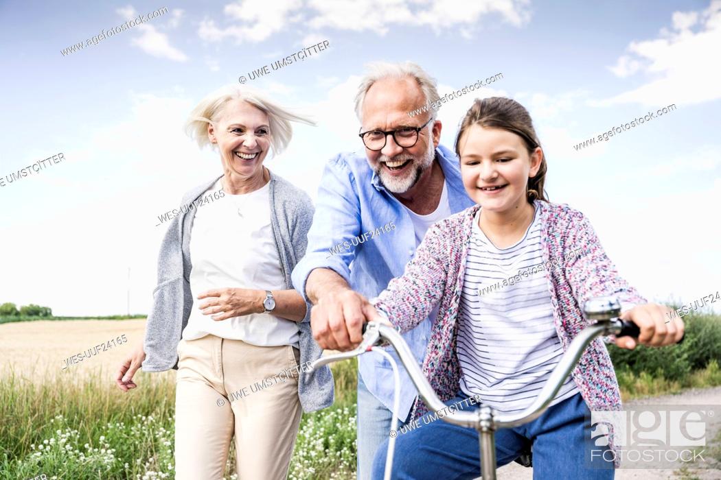Imagen: Smiling grandparents playing with granddaughter riding bicycle.