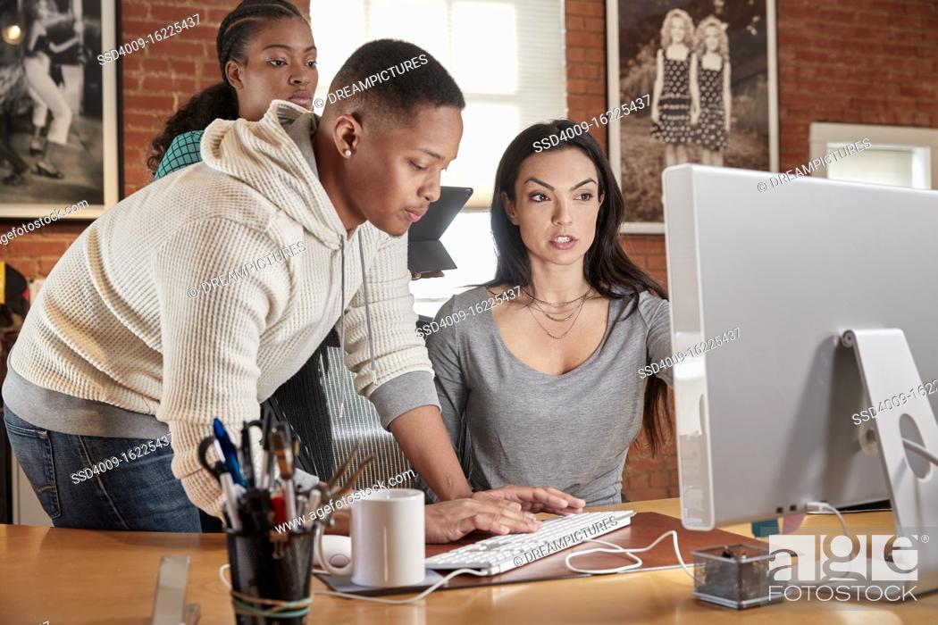 Stock Photo: Group of young co-workers in office gathered around computer screen.