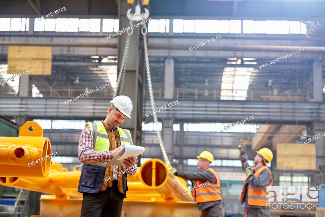 Stock Photo: Male foreman with clipboard standing near workers in factory.