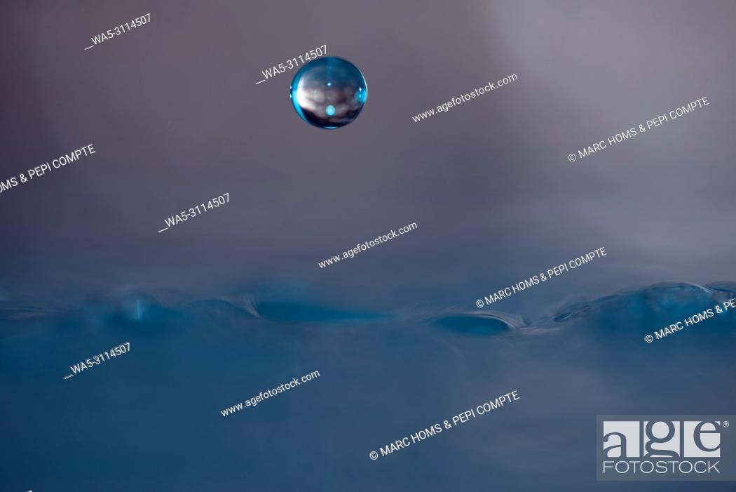 Stock Photo: A drop of blue water suspended above the surface of the water.