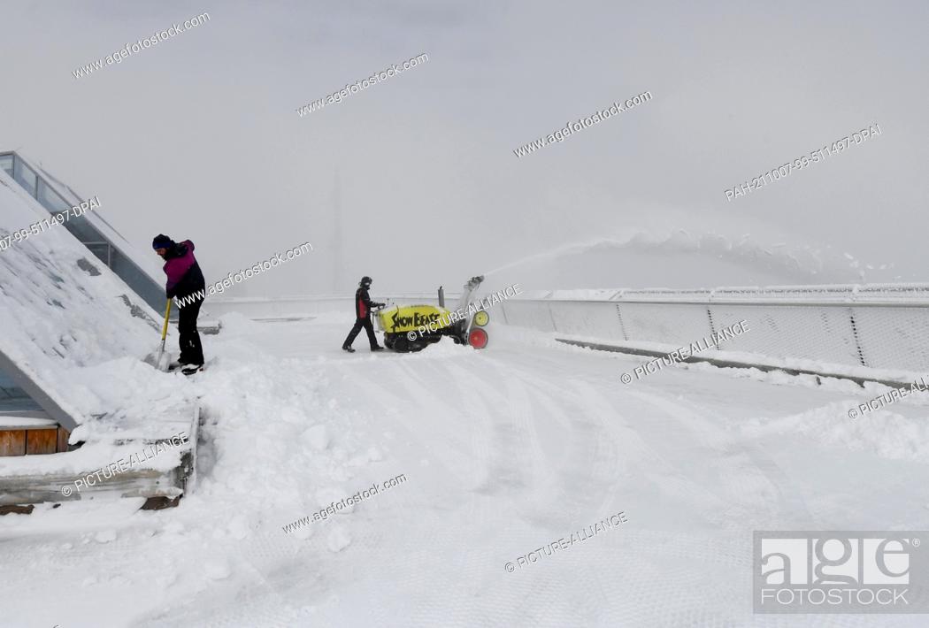 Stock Photo: 07 October 2021, Bavaria, Grainau: Employees clear the roof terrace of the Zugspitze mountain station of snow. In the Alps.