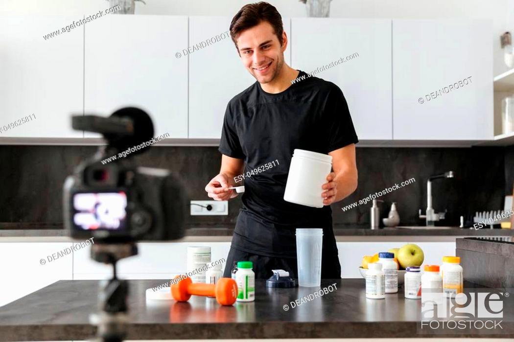 Stock Photo: Happy young man filming his video blog episode about healthy food additives while standing at the kitchen table.