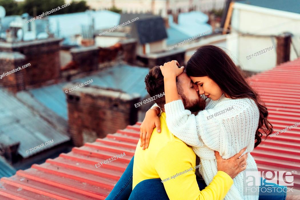 Photo de stock: Loving young couple is sitting on the roof of the house. In the background of a big city house.
