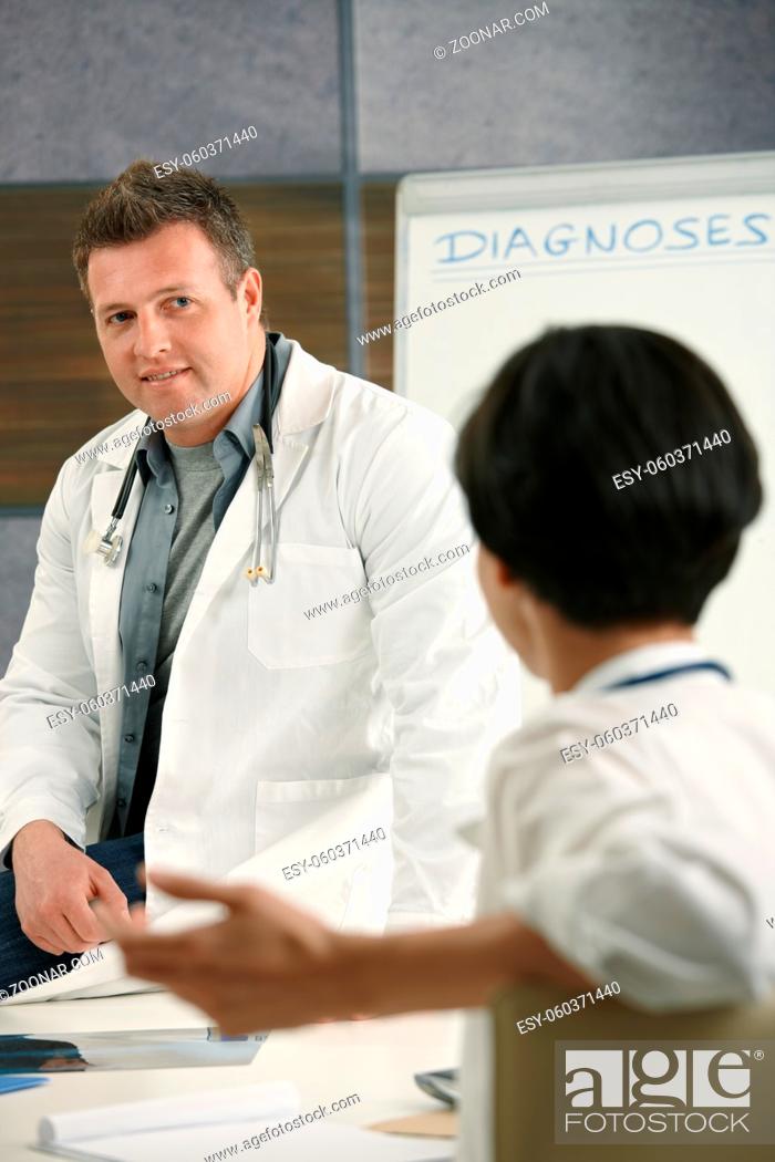 Stock Photo: Two medical doctors chatting in doctor's room, smiling.
