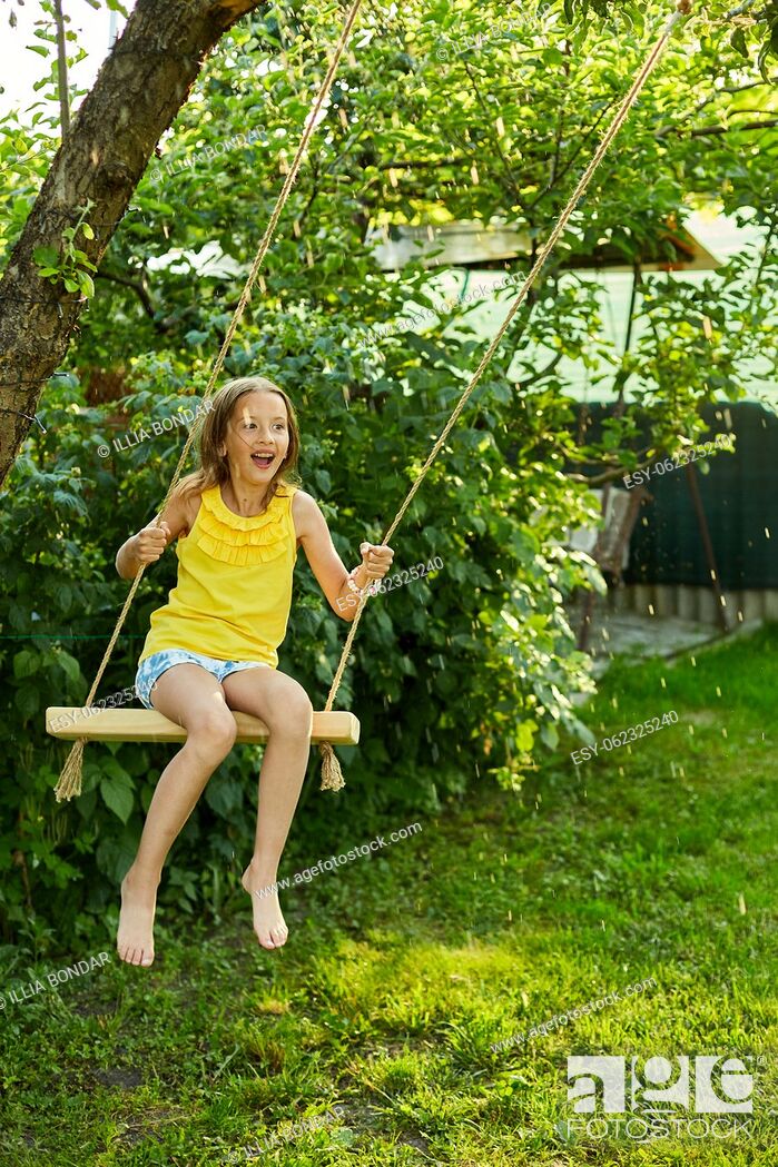 Stock Photo: Happy barefoot laughing child girl swinging on a swing in sunset summer day on the backyard at home, summertime outdoor, vacation.