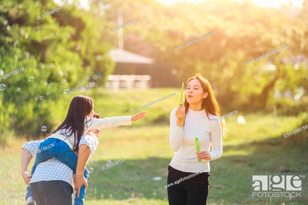 Stock Photo: Happy Asian lifestyle family mother, father and little cute girl child having fun together and enjoying outdoor play blowing soap bubbles in the garden park on.