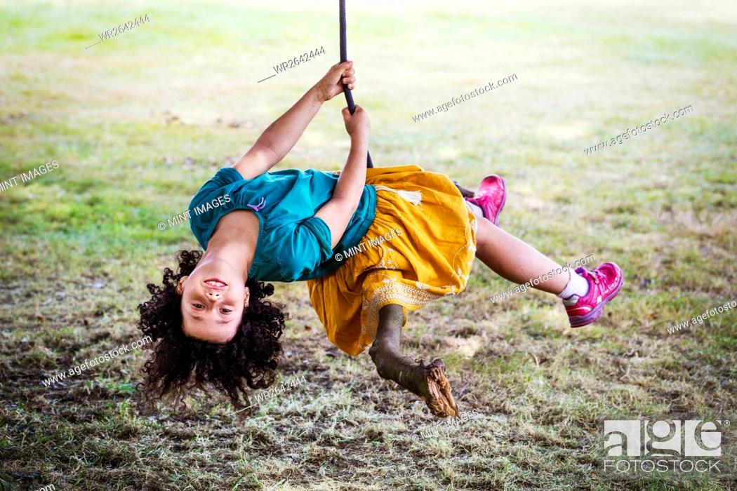 Stock Photo: Girl sitting on a tree swing, upside down, smiling at camera.