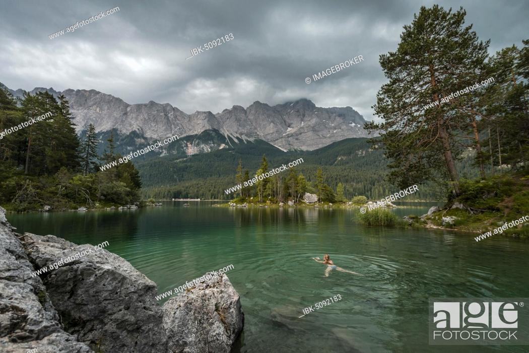 Stock Photo: Woman swimming in the lake, rocks on the shore, view into the distance, Eibsee lake in front of Zugspitze massif with Zugspitze, Wetterstein range, near Grainau.
