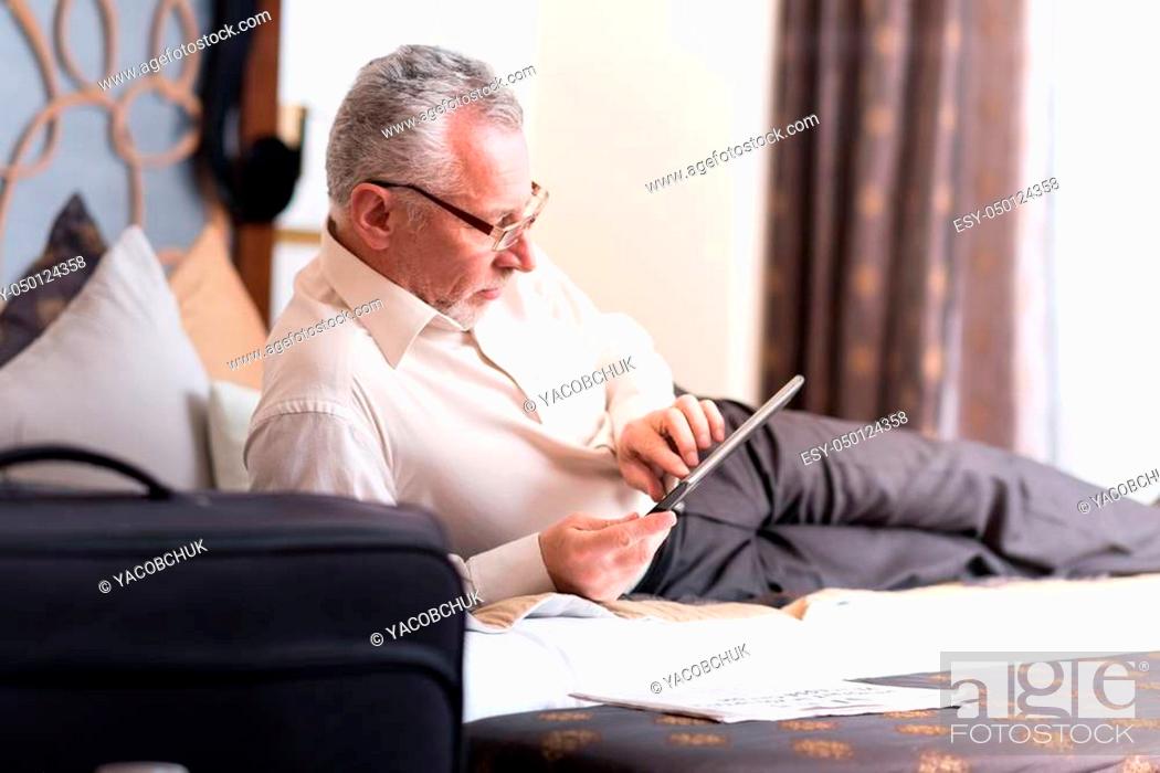 Stock Photo: Get some rest. Delighted senior man lying on the bed and using tablet while resting.