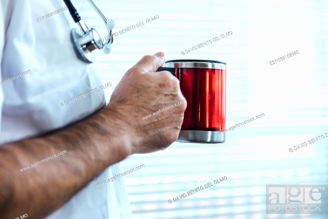 Stock Photo: Mature male doctor - nurse having coffee in a hospital window. Covid-19 and medicine concept.
