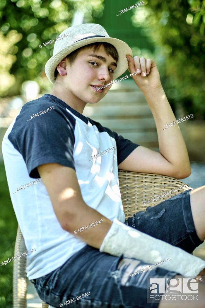 Stock Photo: Portrait of young caucasian boy with a broken and cast arm wearing a hat and sitting in a chair outdoor in a garden. Lifestyle concept.