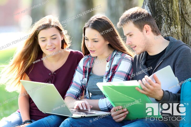 Stock Photo: Three attentive students learning on line together with a laptop and notebook sitting on the grass in a park.