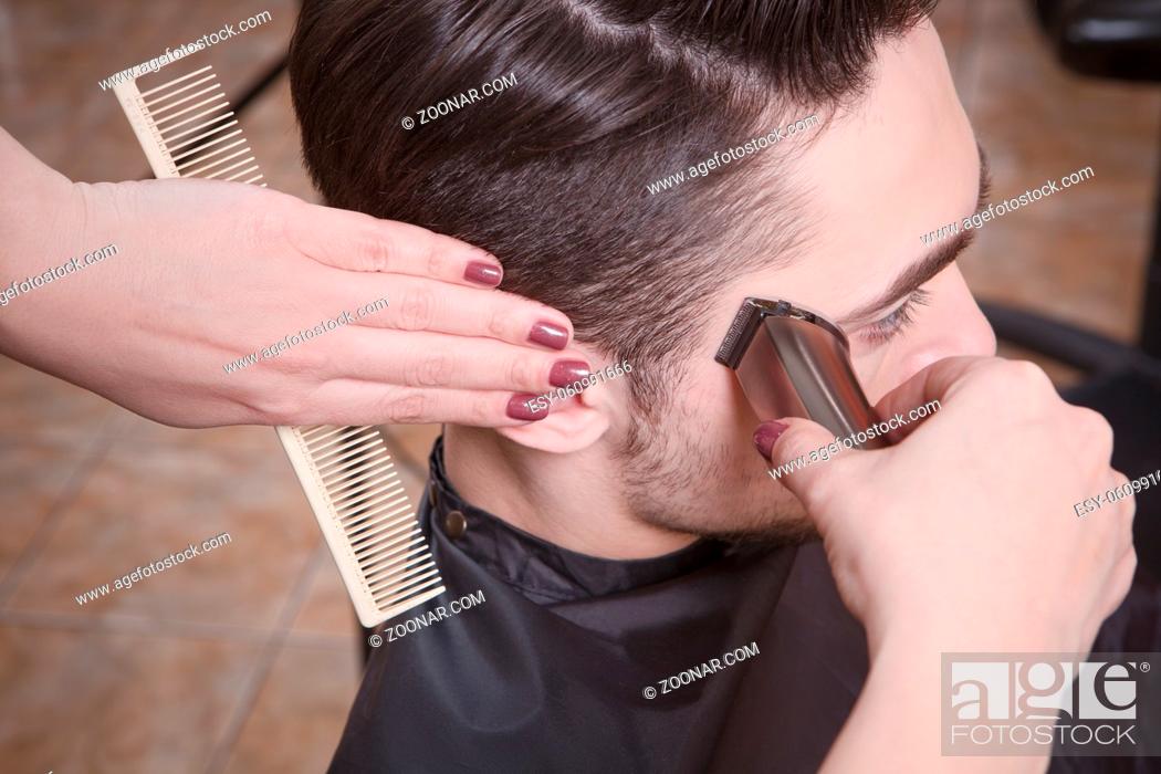 Stock Photo: Closeup picture mas#39;s hairstyling and haircutting with hair clipper by barber girl or hairdresser in barber shop or hairdressing salon.