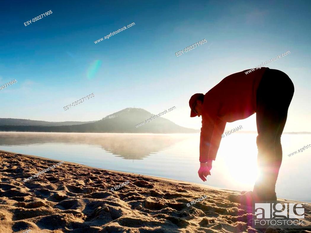 Stock Photo: Man exercising on the beach. Silhouette of active man exercising and stretching on the lake beach at sunrise. Healthy lifestyle.