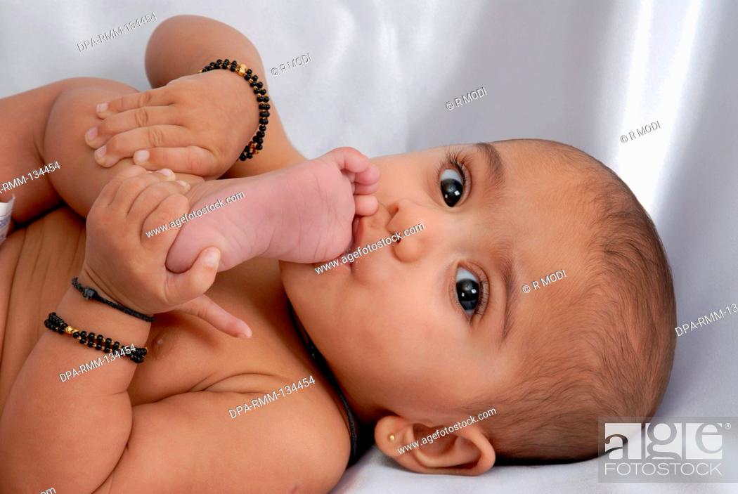 Stock Photo: South Asian Indian baby , chewing the toe in her mouth , looking at camera , white background , India MR152.