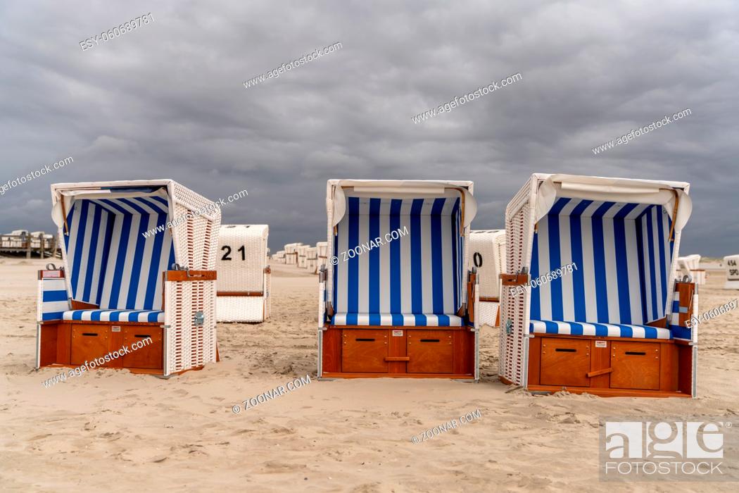 Stock Photo: colorful beach baskets on an idyllic golden sand beach on the German Wadden Sea coast under an expressive sky.