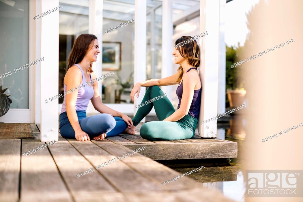 Stock Photo: Female friends talking while sitting by columns on hardwood floor.