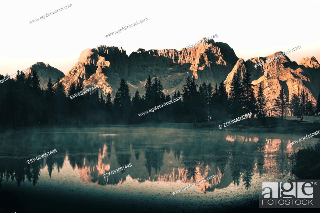 Stock Photo: Mountains and sky reflection in a lake with forest in the dolomites during sunrise with fog on the water.