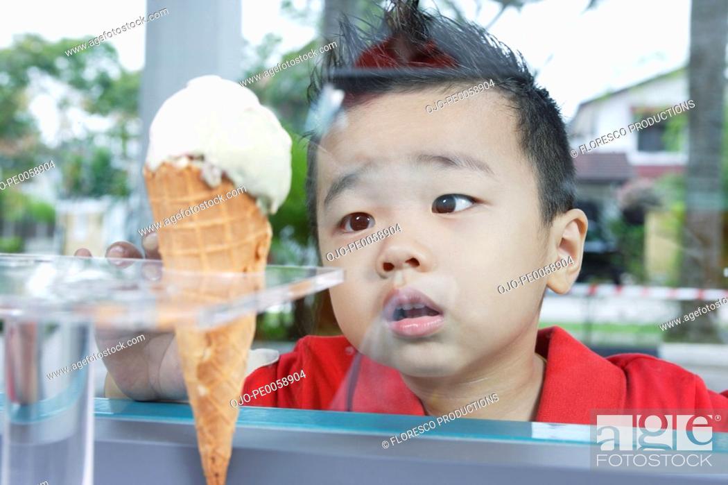 Stock Photo: Boy looking at ice cream cone through glass.