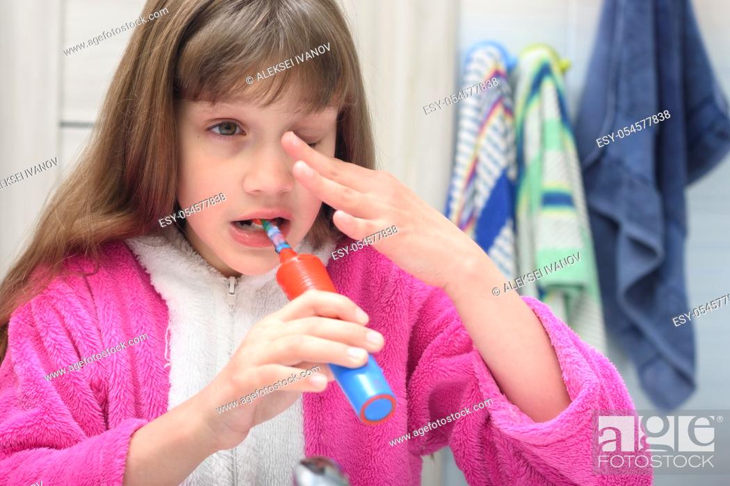 Imagen: Sleepy girl brushes her teeth in the early morning.