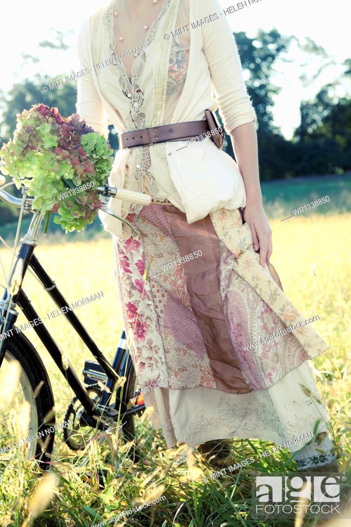 Stock Photo: A girl in vintage clothing, paisley patterned cotton skirt with a bicycle in long grass.