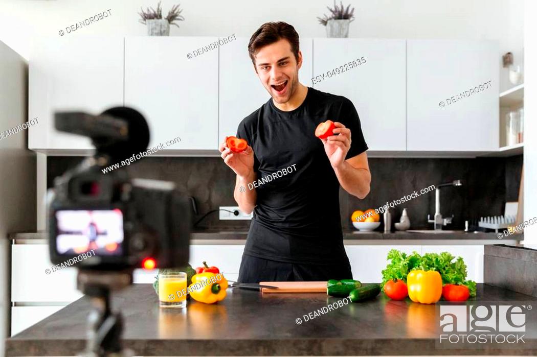 Stock Photo: Joyful young man filming his video blog episode about healthy food cooking while standing at the kitchen table.