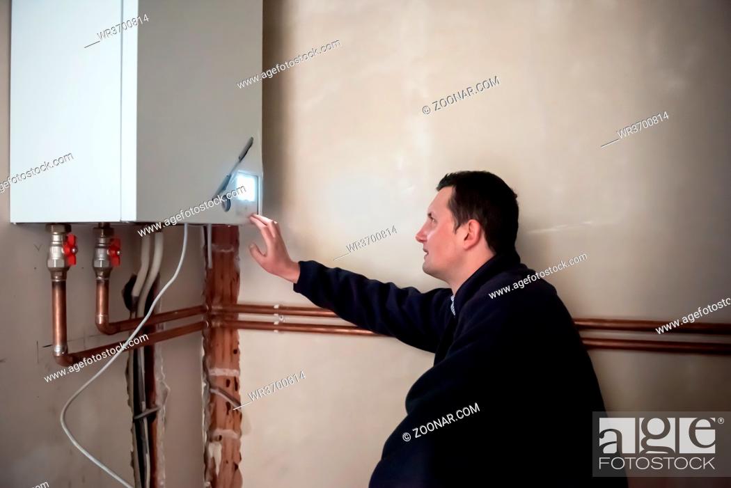 Stock Photo: Maintenance engineer checking technical data of heating system equipment in a boiler room. Plumber installing pressure meter for house heating system.